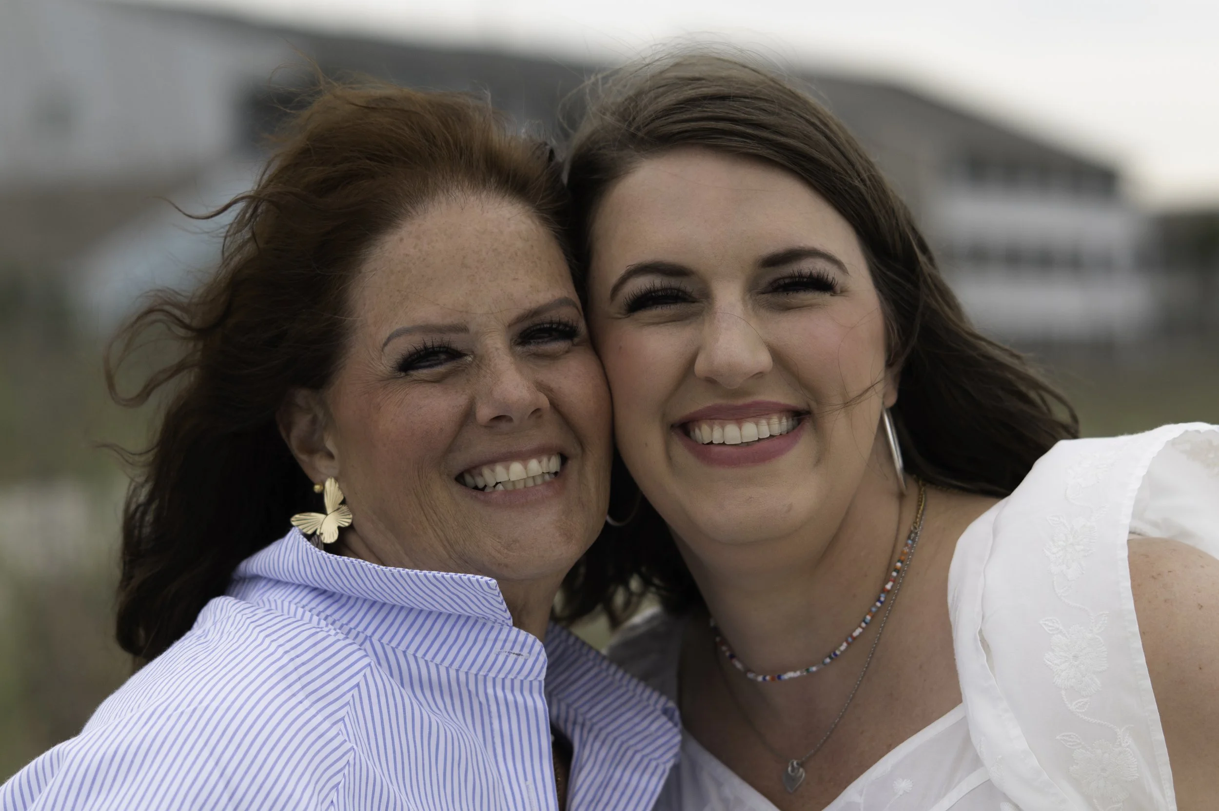 Two women smiling, close-up of their faces, outdoors, in front of a blurred background.