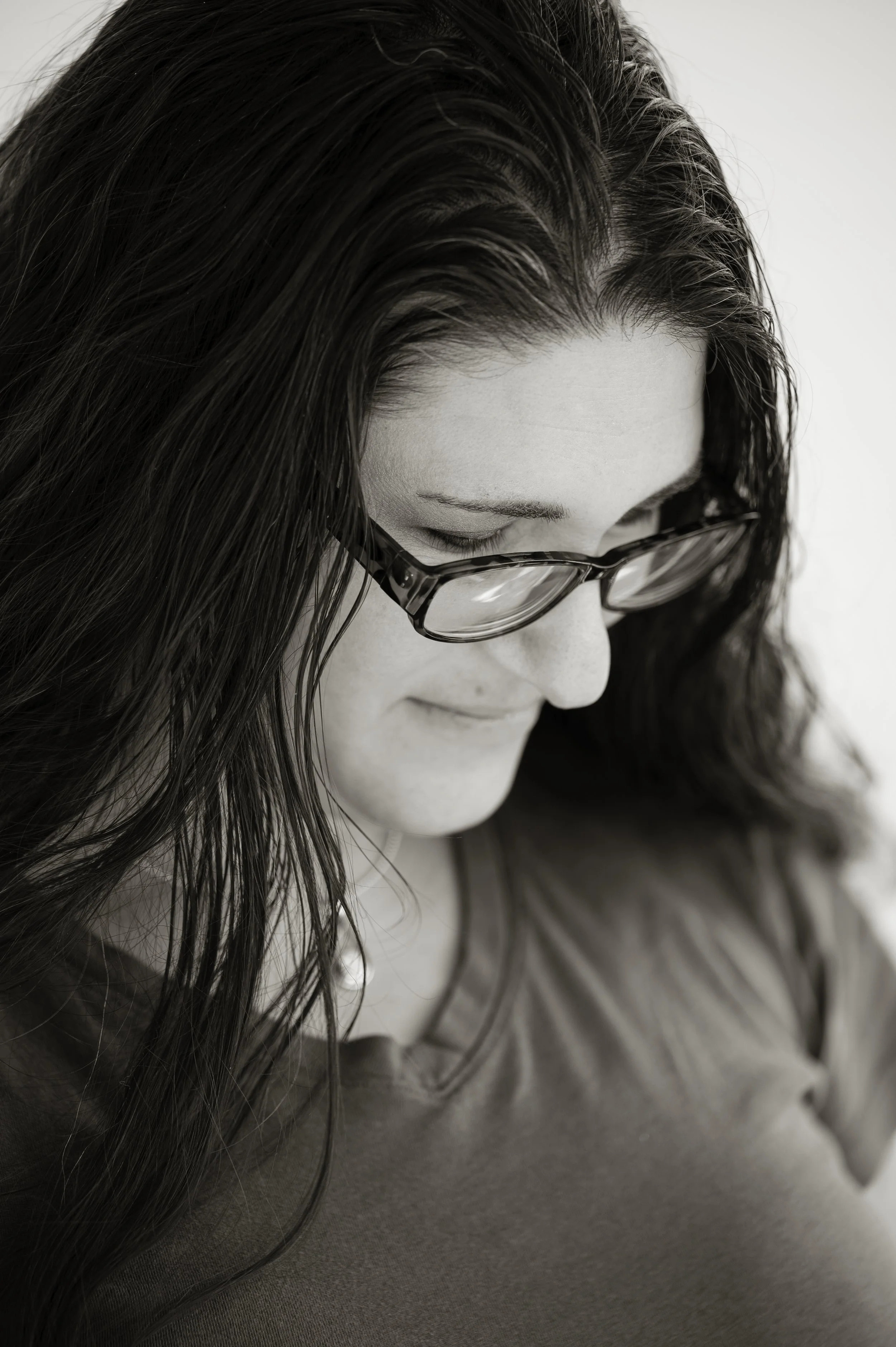A woman with long dark hair and glasses looking down and smiling.