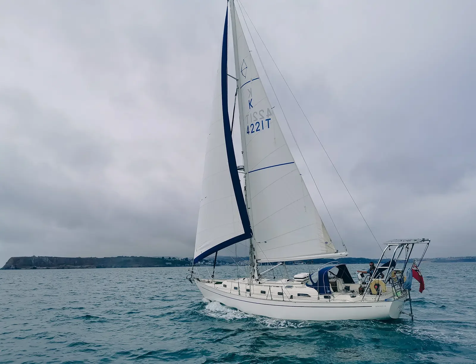 Yacht sailing on the ocean on a cloudy day with land visible in the background.