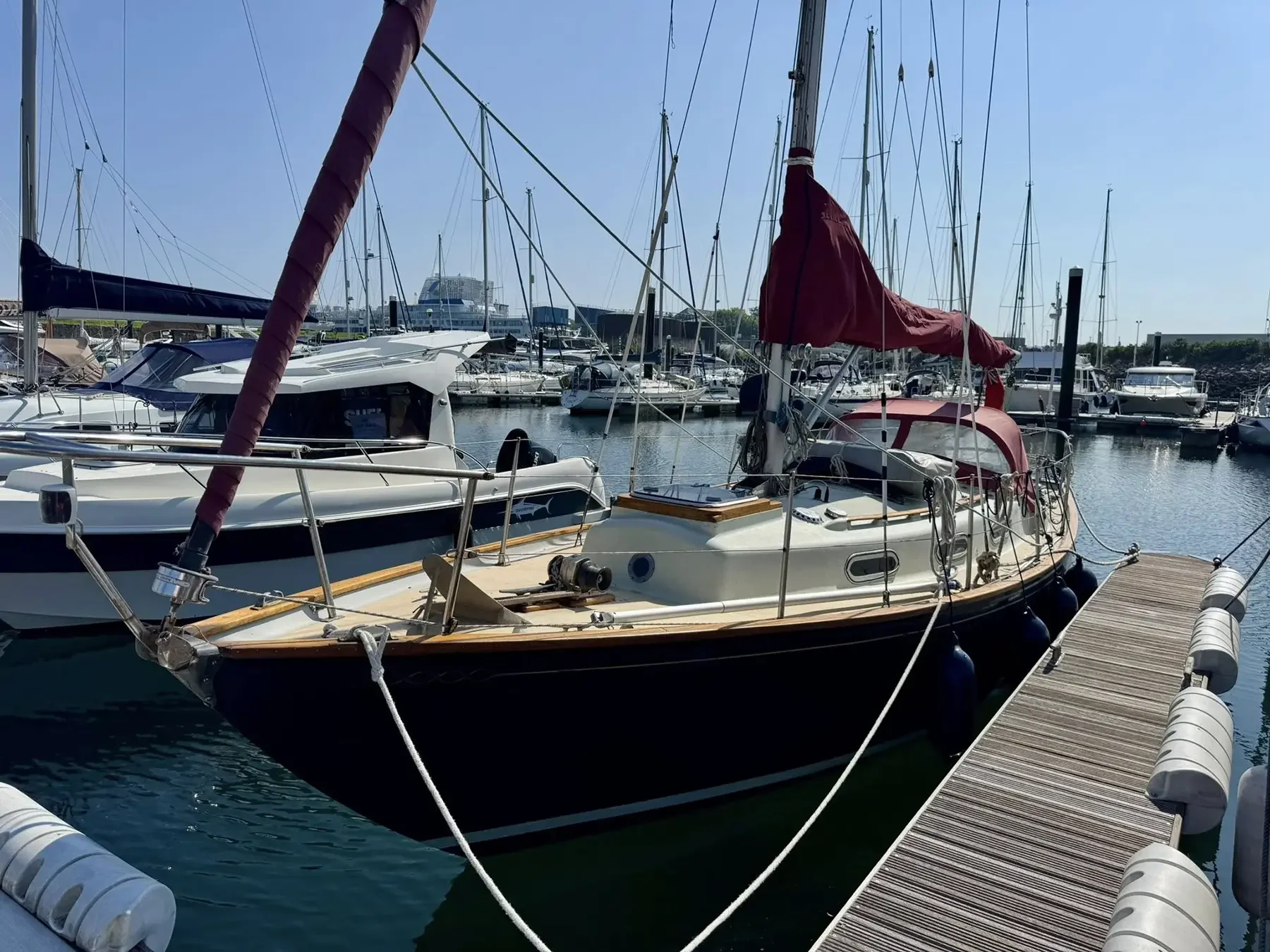Sailing yachts docked at a marina with calm water, a clear sky, and a wooden pier on the right side.