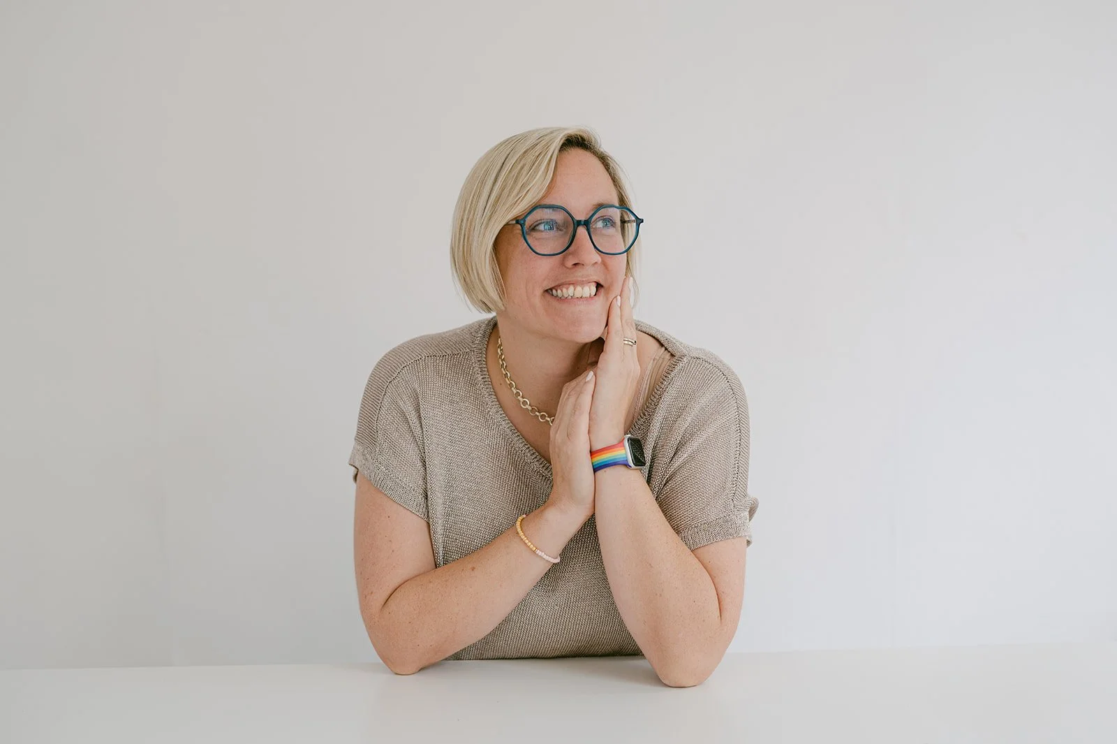 A portrait shot of Kate Faxen in muted colours and smiling broadly. She has a short blond bob and is wearing turquoise framed glasses.