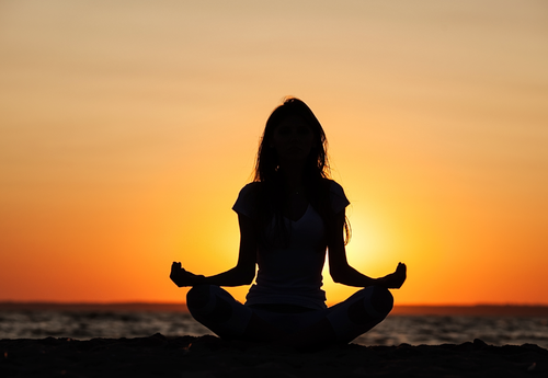 Silhouette of a woman meditating on the beach at sunset.