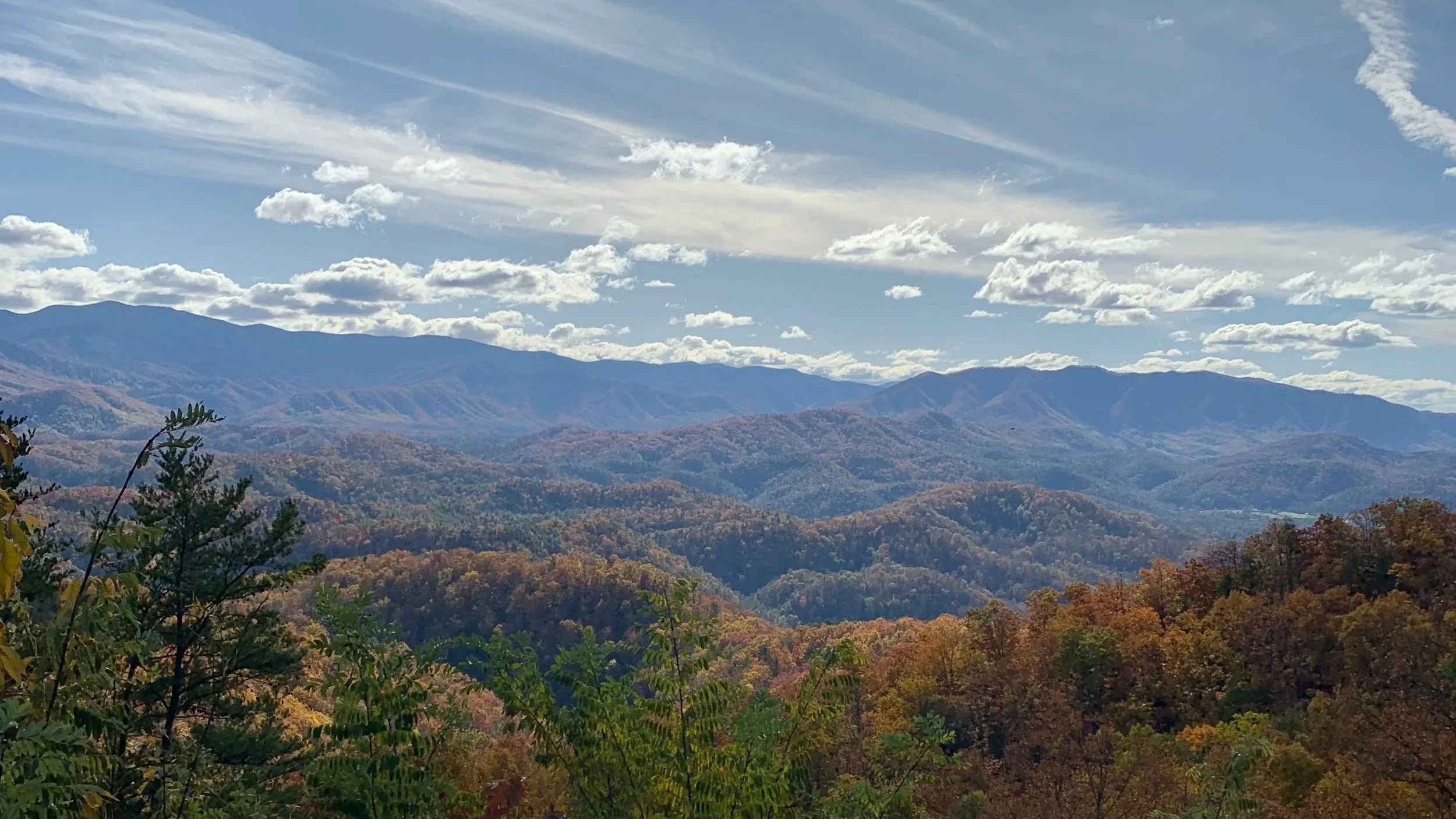 Scenic view of mountain range with rolling hills covered in fall foliage, under a partly cloudy sky.