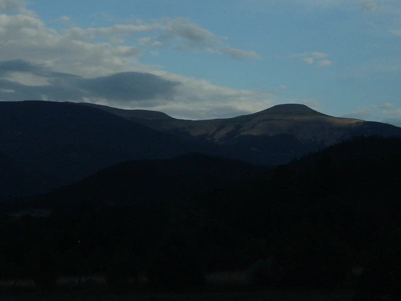 A mountain range under a partly cloudy sky with shades of blue and grey.