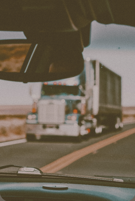 photo taken from inside a moving vehicle shows a semi-truck ahead on the highway, visible through the windshield and rearview mirror