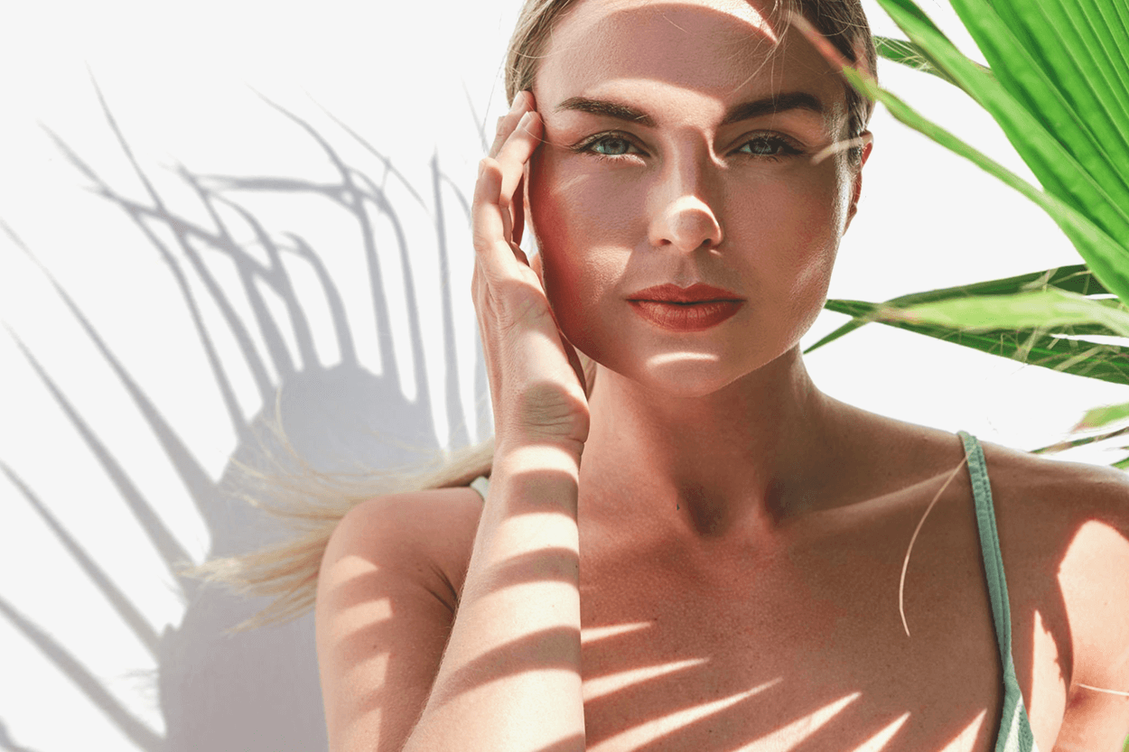 image of a beautiful woman's face under the shade of a tropical palm branch.