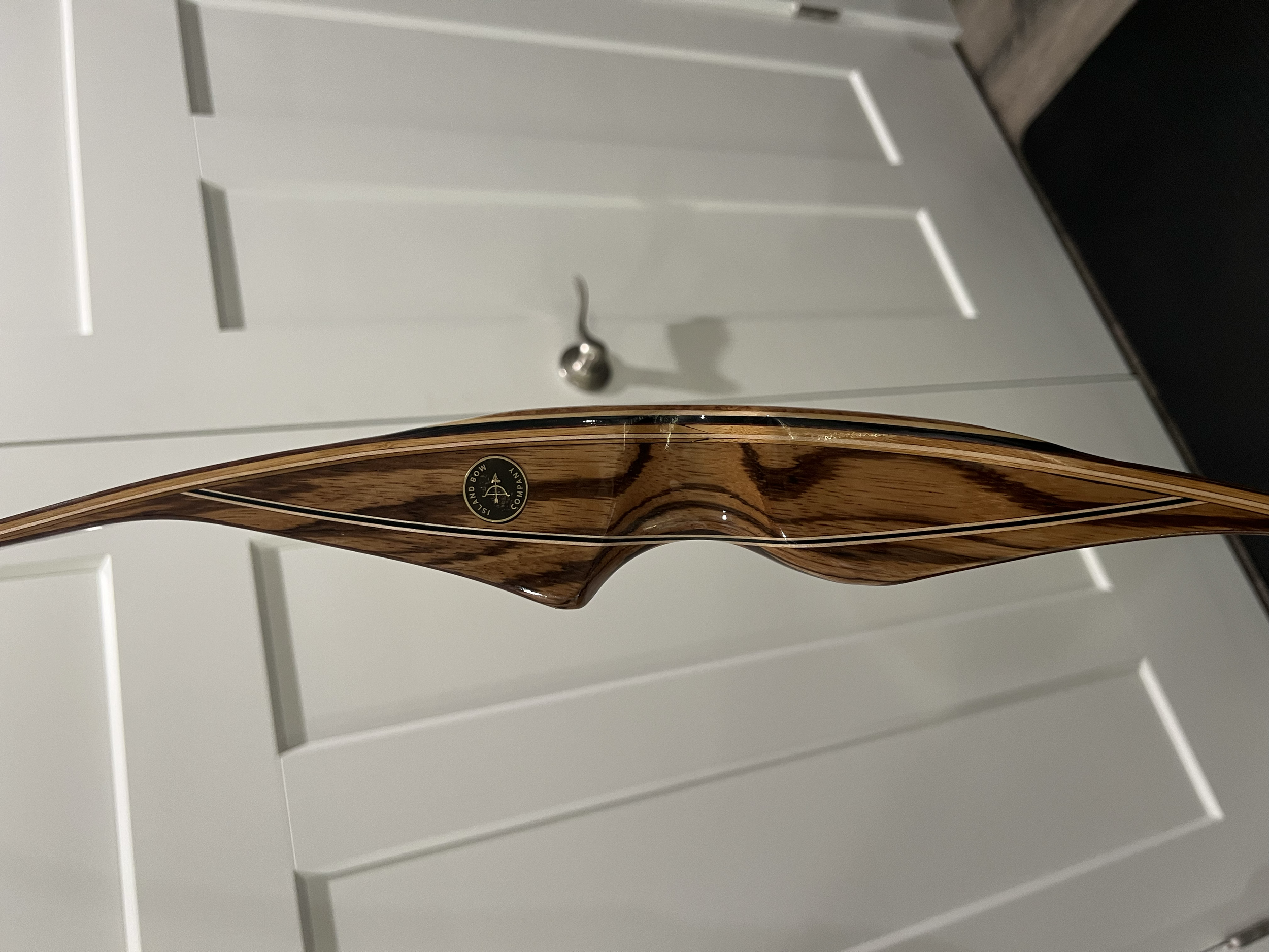 A wooden archery bow with a logo, mounted on a white cabinet door.