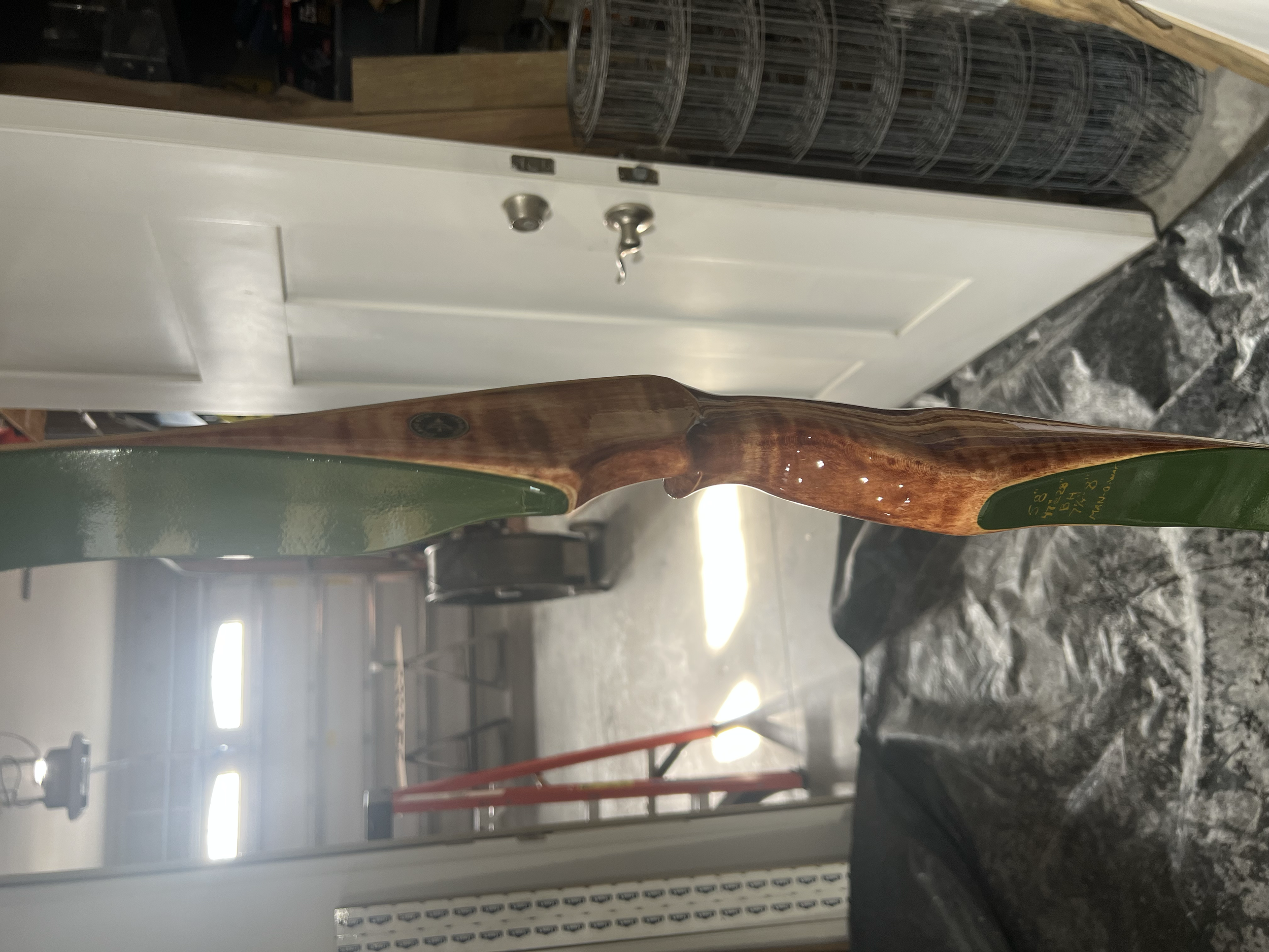 Close-up of a wooden hockey stick with green tape on one end, positioned indoors near a closed white door and various objects in the background.