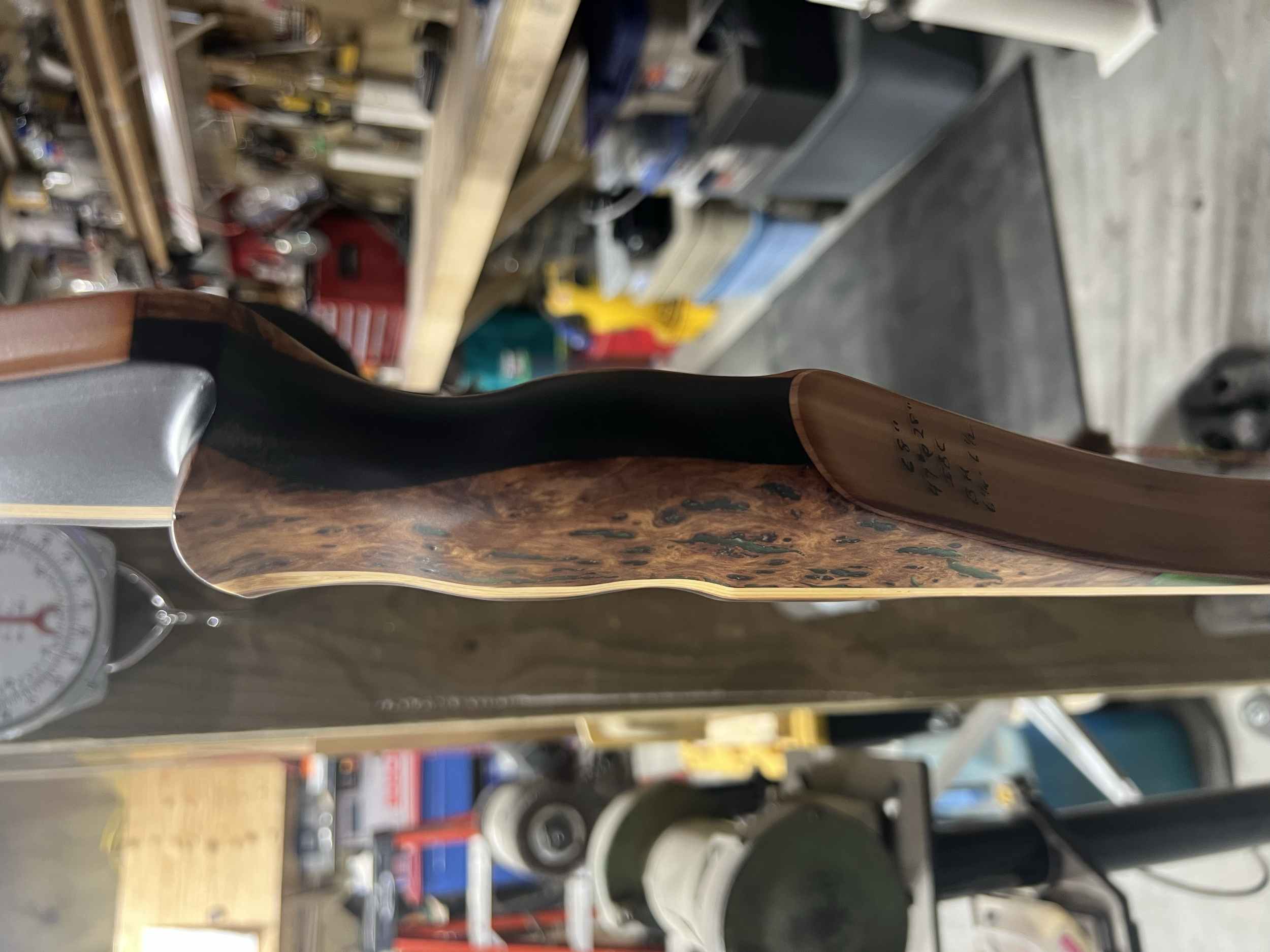 Close-up side view of a wooden bow with a black grip, in a woodworking or workshop setting.