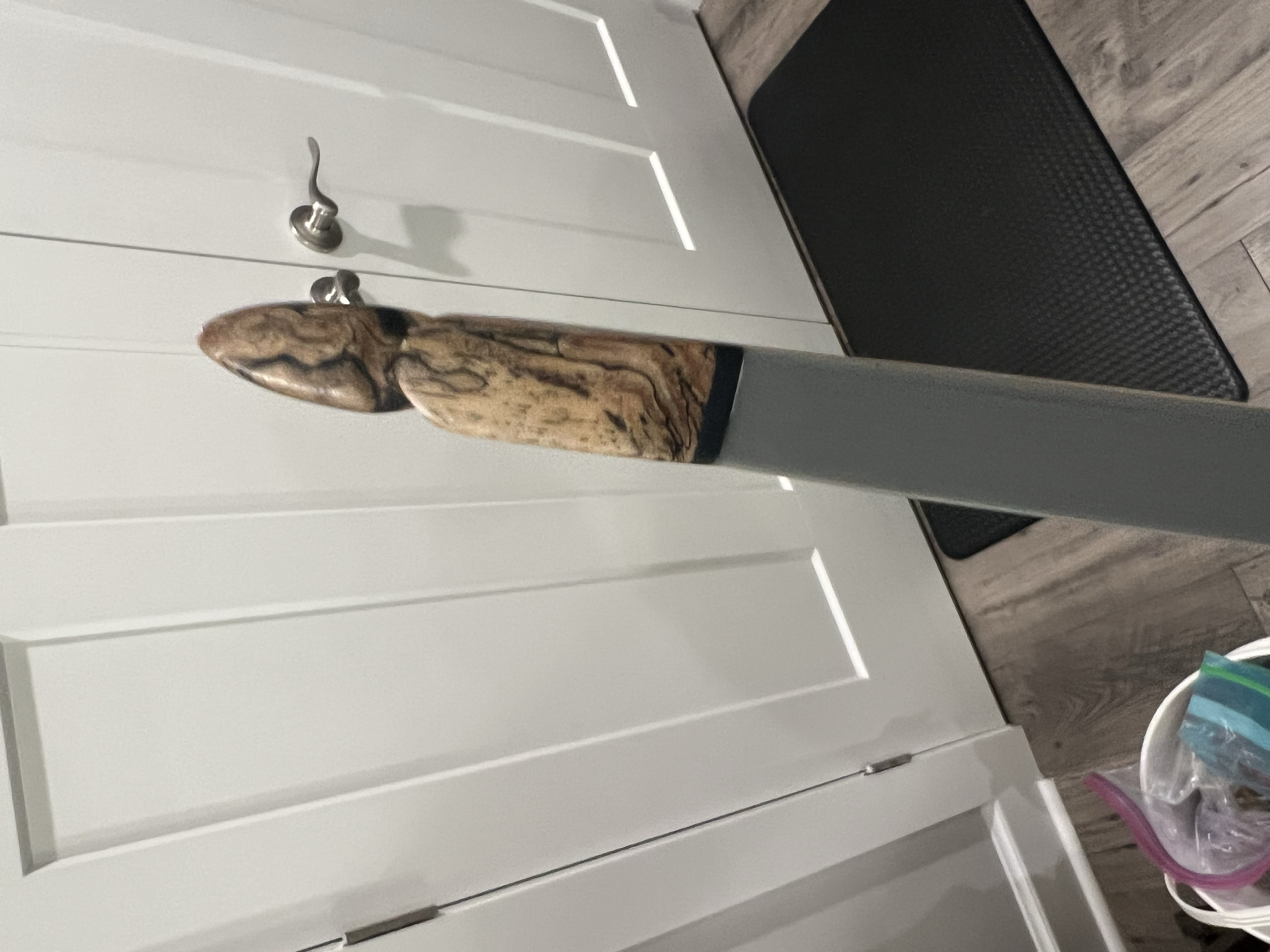 Decorative wooden object mounted on a black stand, placed in a room with white panel doors, a black mat, and a gray floor.