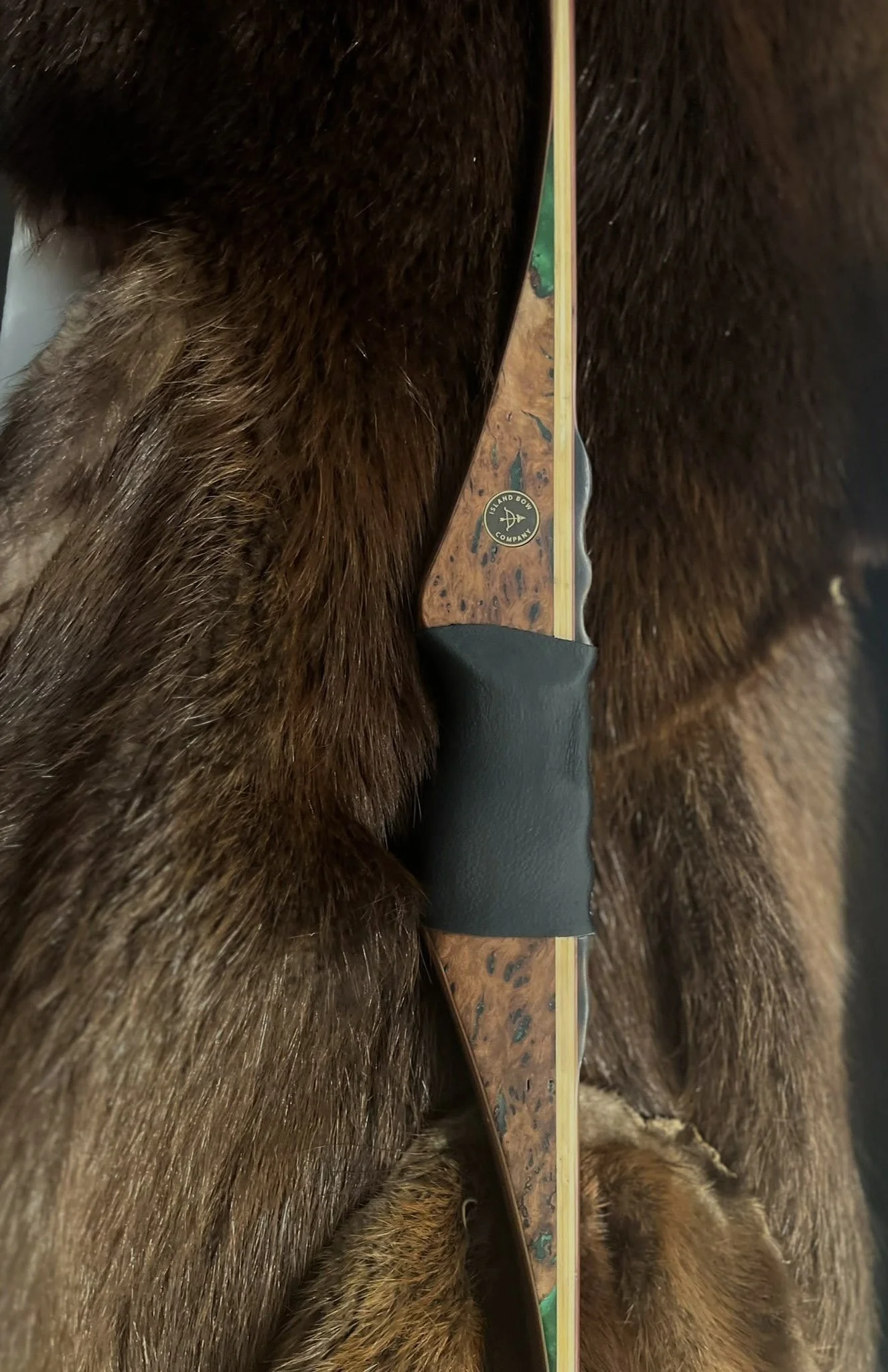 A bow with a wooden handle and string, partially concealed by brown fur.