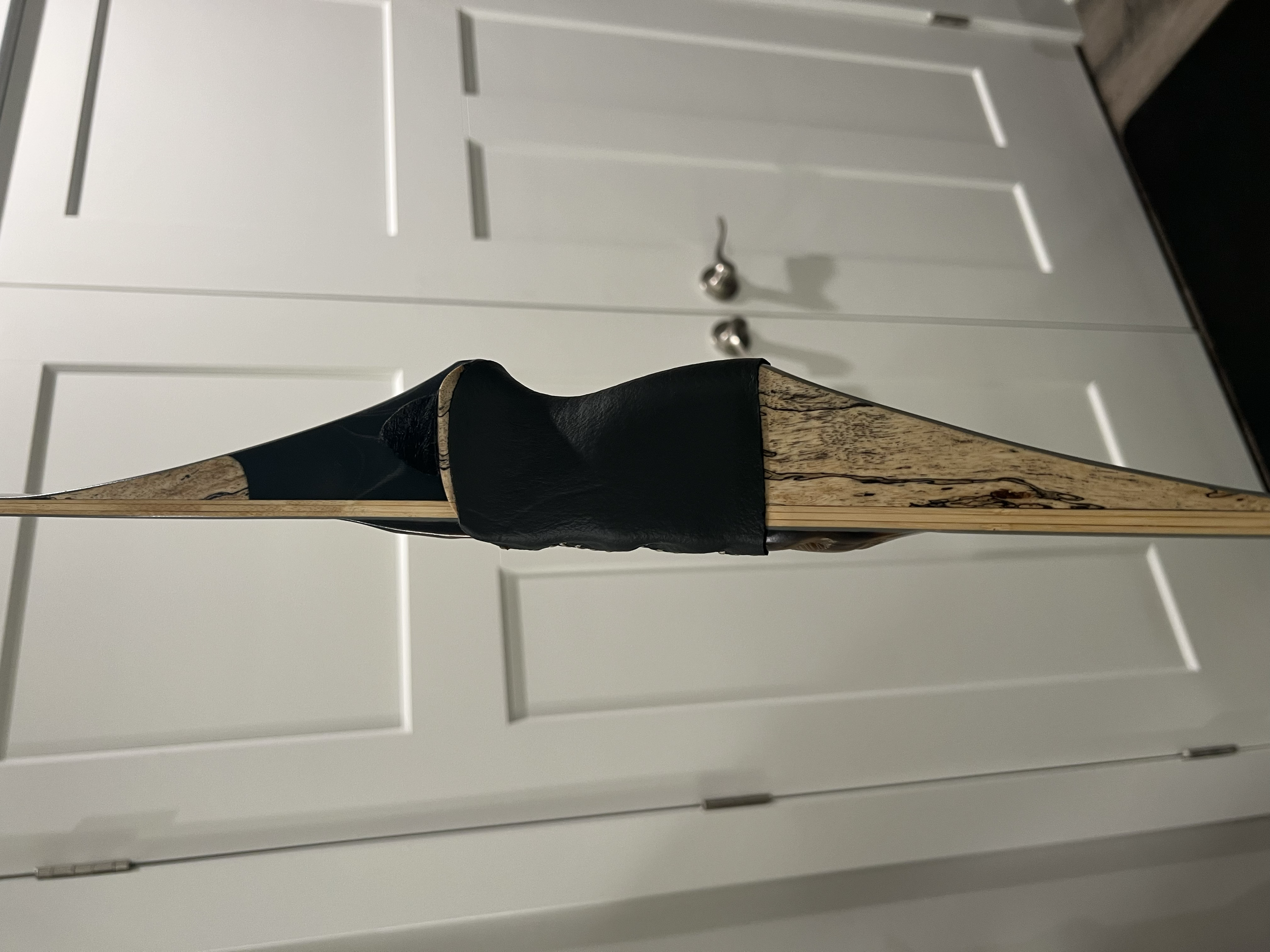 Close-up of a wooden stand with a leather-covered tip, possibly a bow for archery, with a white cabinet with silver handles in the background.