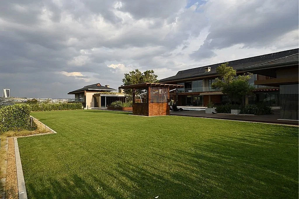 A modern residential building with a large green lawn, trees, and a cloudy sky.