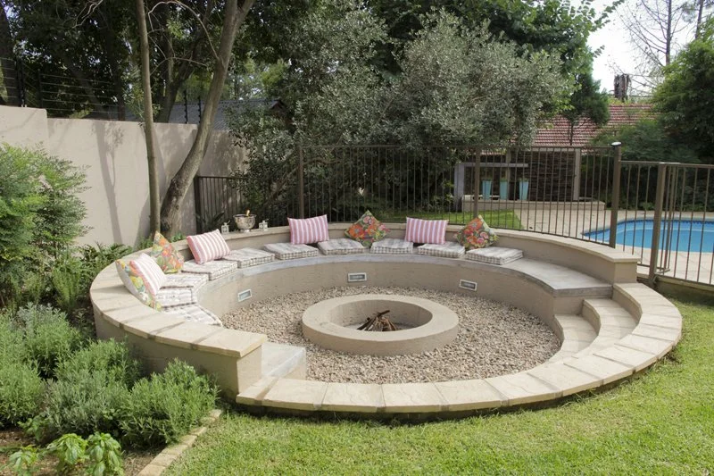 Sunken circular fire pit with herb planting and water feature backdrop