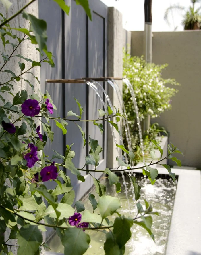 Bespoke built water feature with copper spouts and small pond softened by flowering shrubs