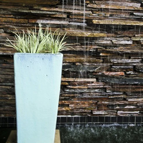 Bespoke water feature with water cascading over slate wall and glazed clay plater with aquatic planting