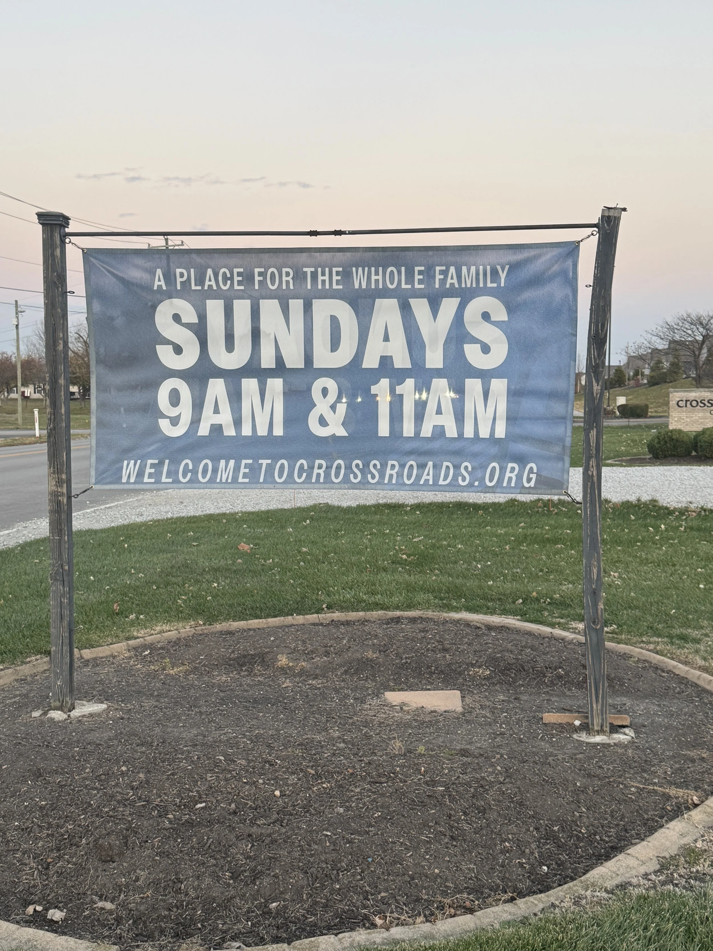 A sign outside a church or community center advertising Sunday service times at 9 AM and 11 AM, promoting a family-friendly environment, with the website welcometocrossroads.org.