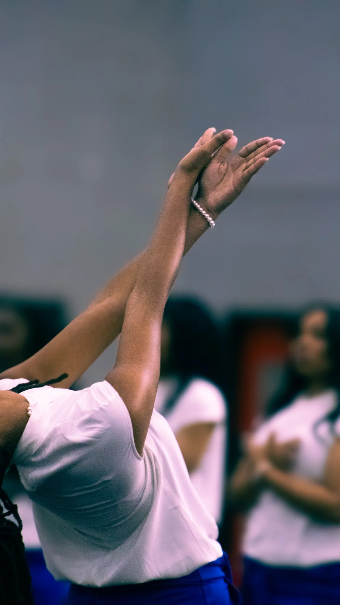 A person with raised hands, wearing a pearl bracelet, during a group activity or gathering.