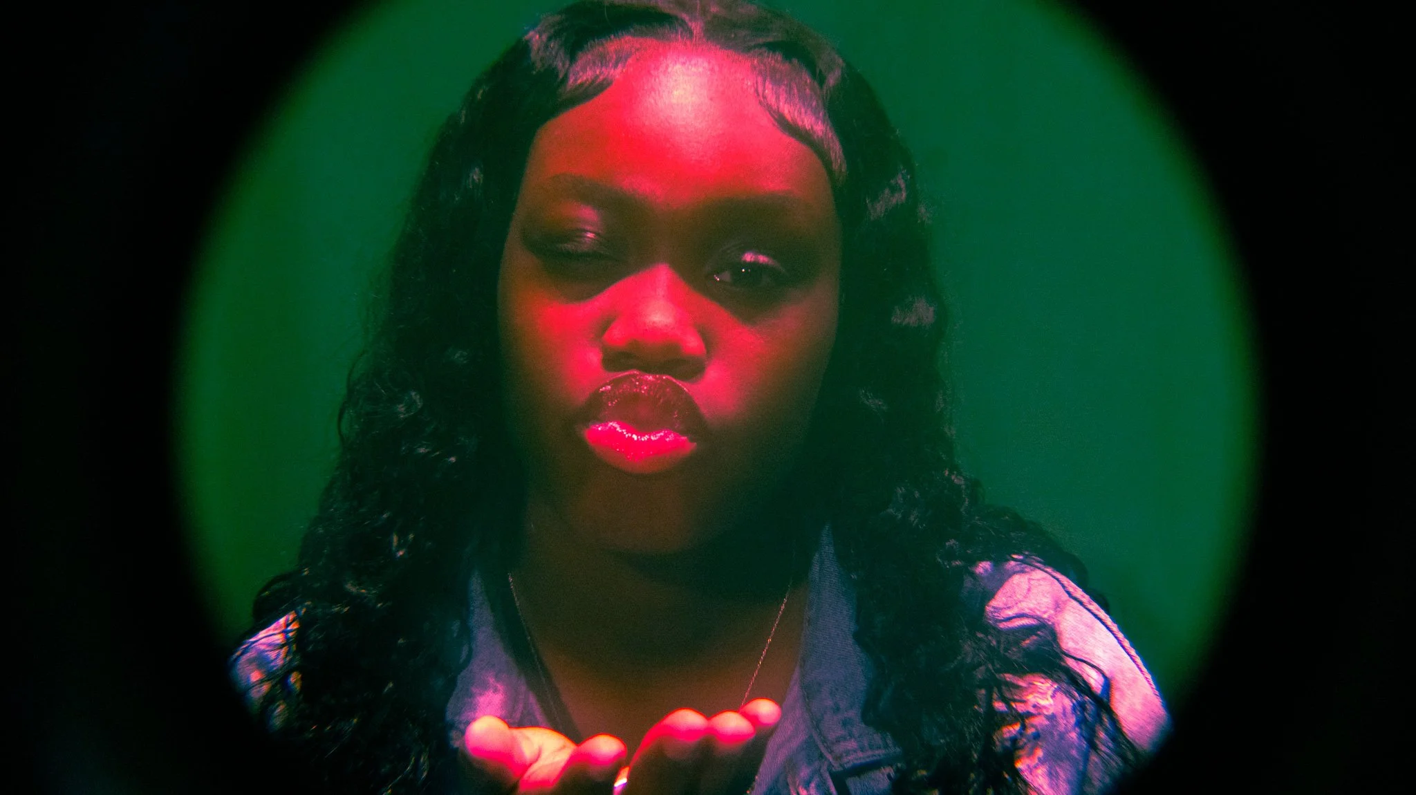 A woman with dark skin and curly black hair blowing a kiss toward the camera.