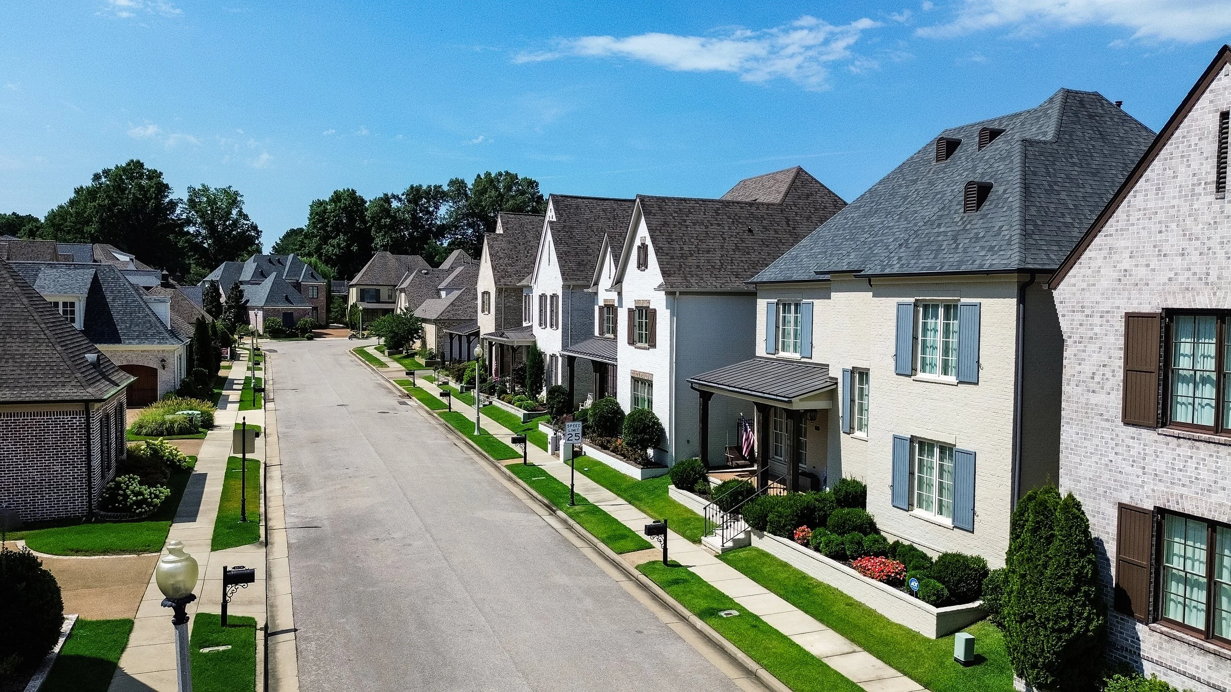 A quiet suburban street in the Somerset neighborhood in Lakeland, TN lined with modern houses with well-maintained lawns and trees, under a clear blue sky.