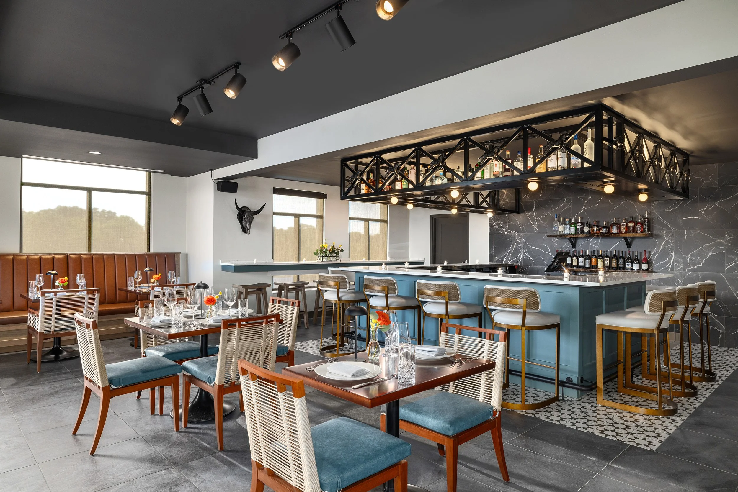 Interior of the Overland restaurant in Germantown, TN with tables set for dining, decorated with flowers, featuring a bar area with liquor bottles. The space has a dark ceiling with track lighting and large windows letting in natural light.