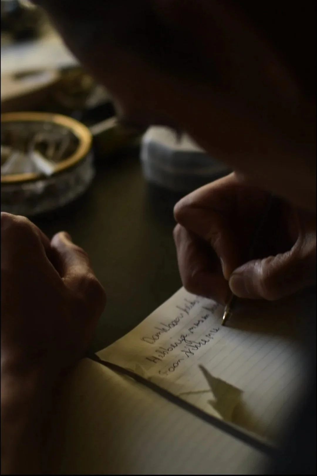 Person writing on a notepad with handwritten text, in a dimly lit environment.