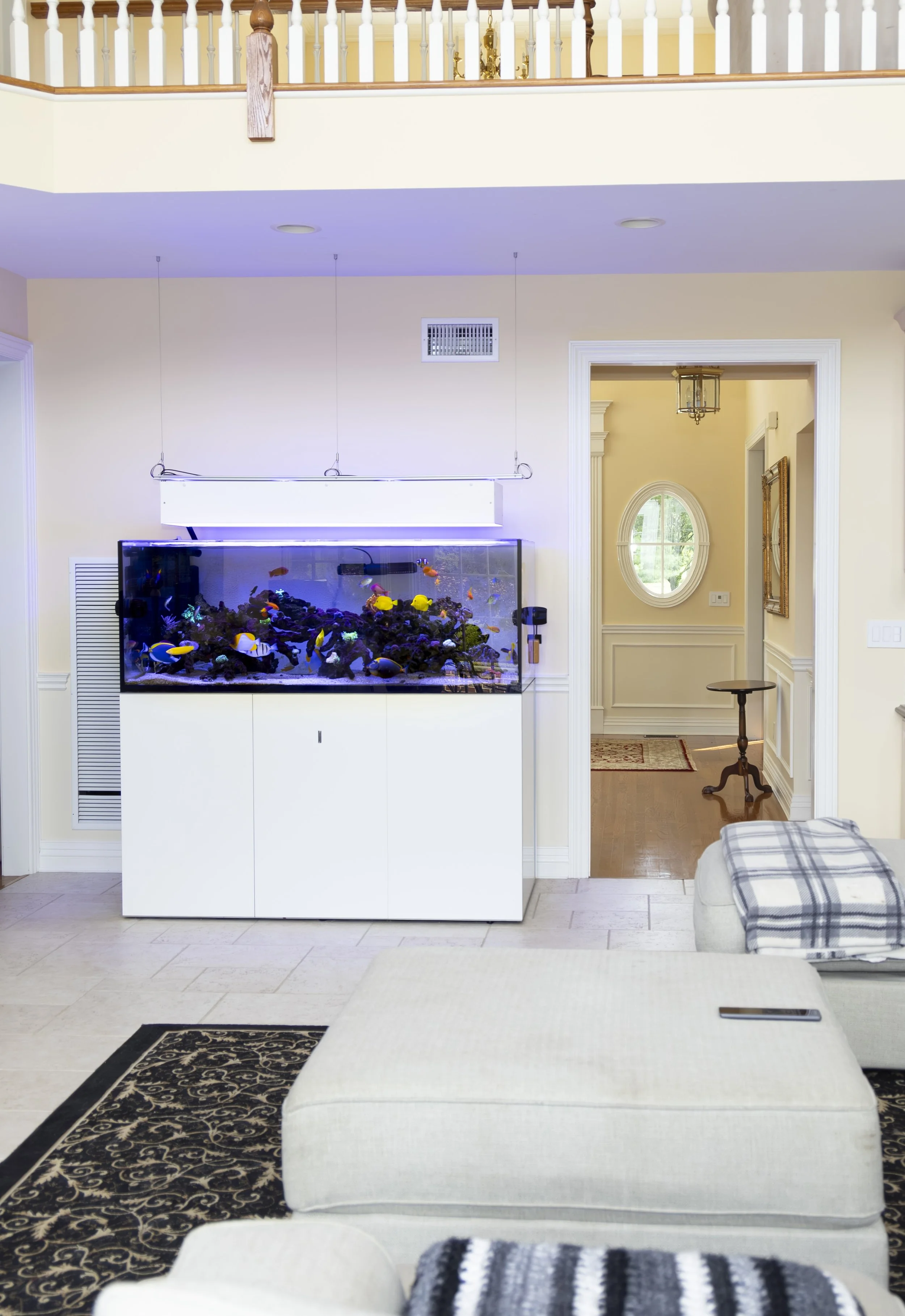 a freestanding custom saltwater aquarium in a bright, open residential living space, showcasing a thriving coral reef and colorful tropical fish as a serene focal point within a warm, modern home interior.
