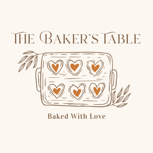 An illustration of a baking tray with six heart-shaped cookies, decorated with a darker heart pattern inside, surrounded by leaves. Text reads 'The Baker's Table' at the top and 'Baked With Love' at the bottom.