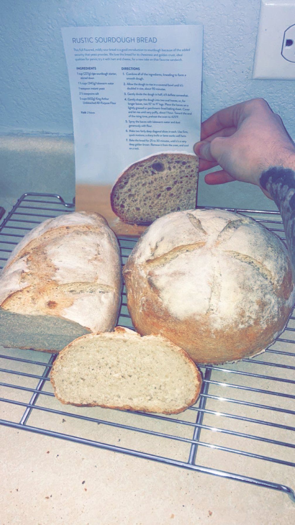 Fresh rustic sourdough bread on a cooling rack, with some slices cut and a loaf picture in the background, along with a recipe for the bread.