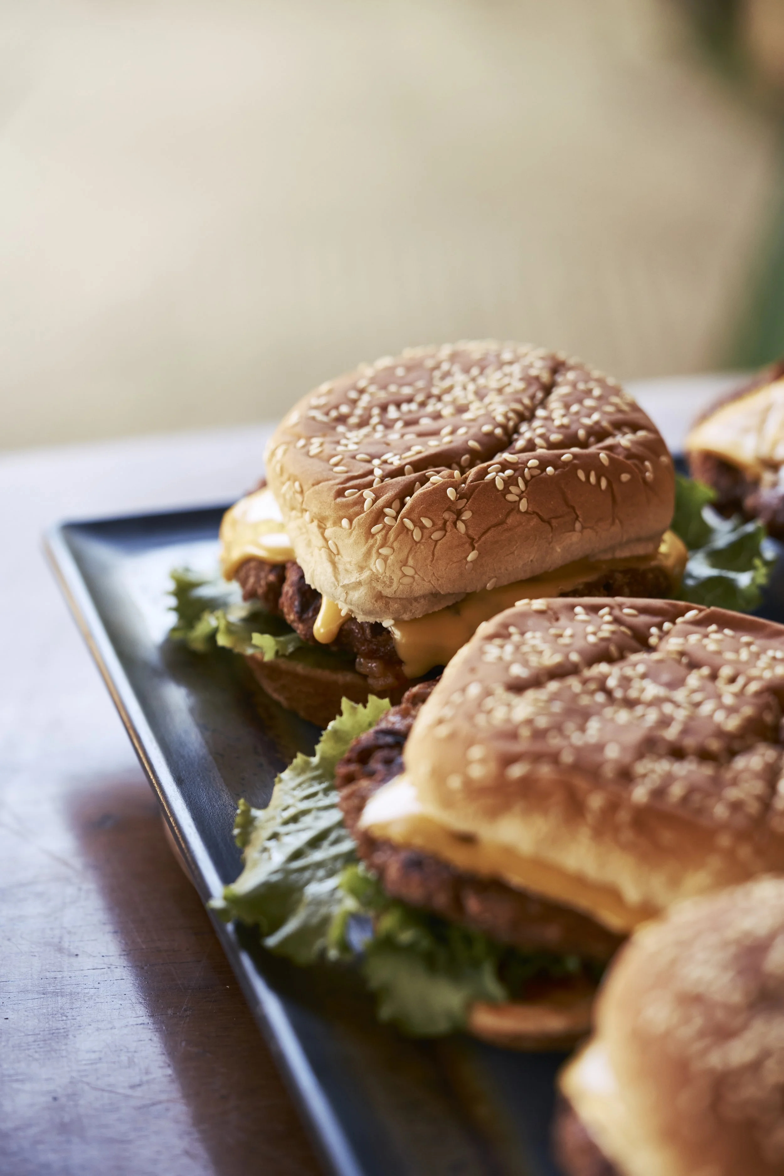 Hamburguesas con pan con semillas de sésamo, carne, queso, lechuga y otros ingredientes, servidas en un plato negro sobre una mesa de madera.