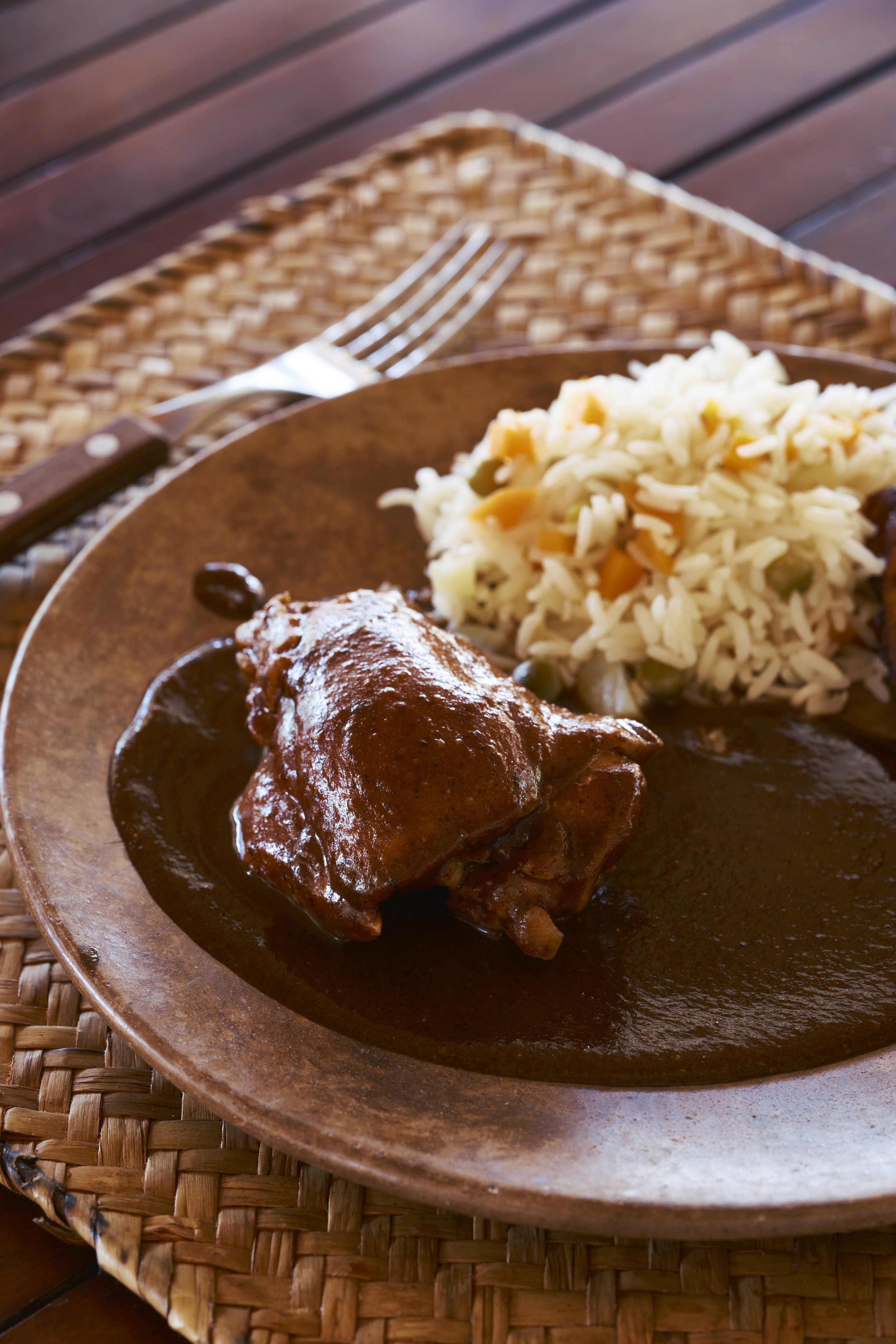 Plato de comida con costillas en salsa, arroz con verduras y guarniciones, en una mesa de madera con tenedor.