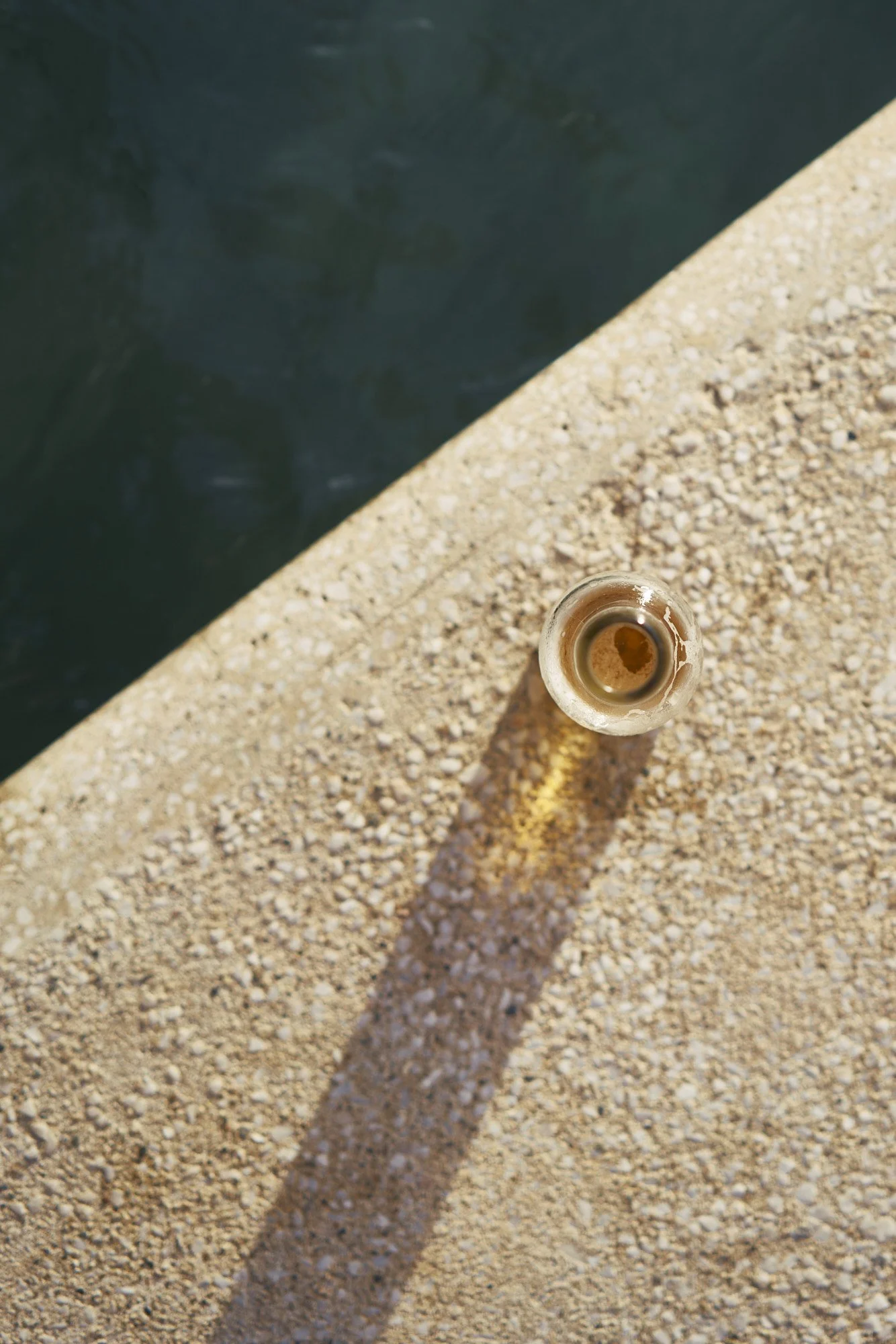 Vista aérea de una botella vacía en una superficie de piedra cerca del borde de una piscina con agua.