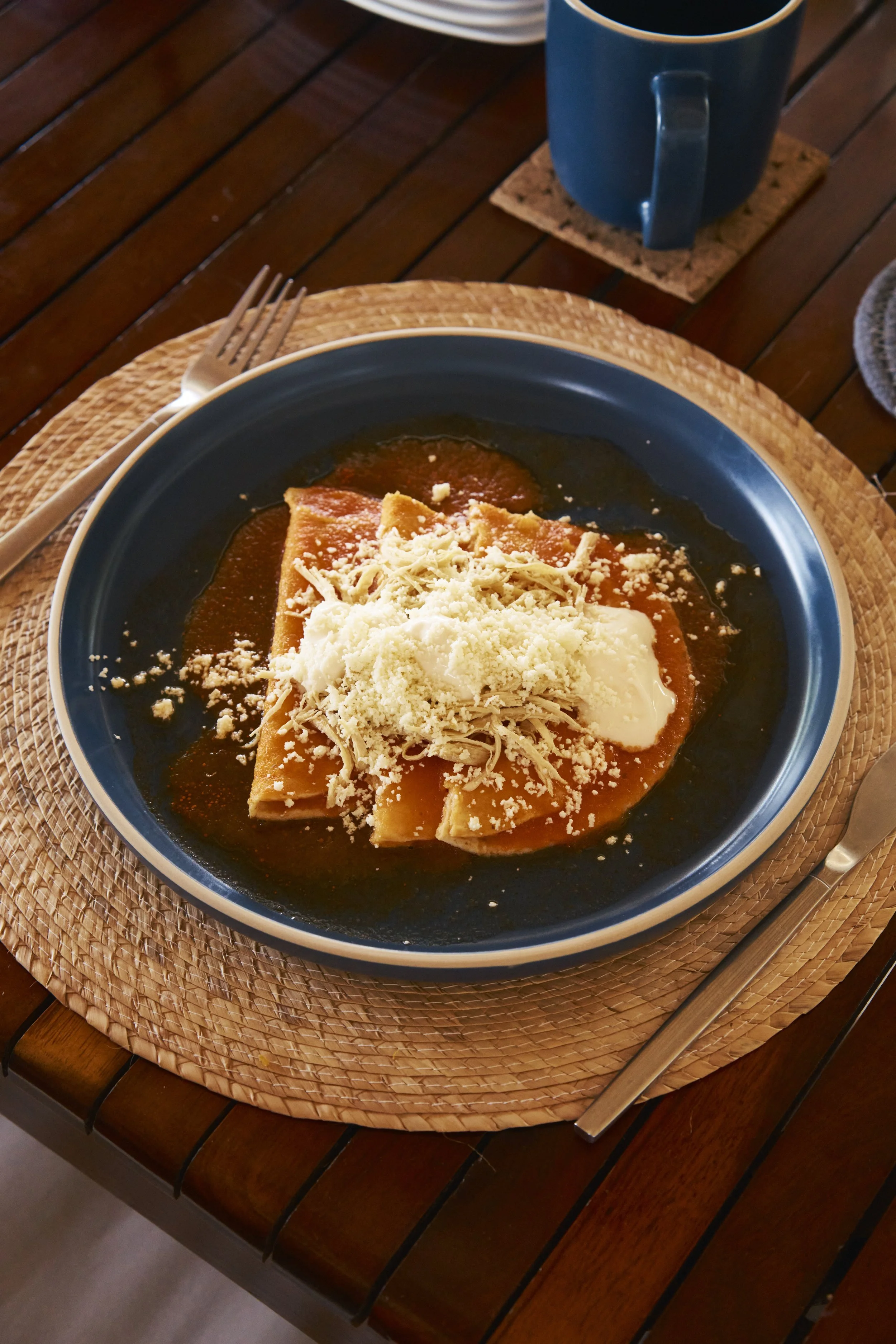Plato de tamales cubiertos con queso rallado y una salsa en un plato azul sobre una mesa de madera.