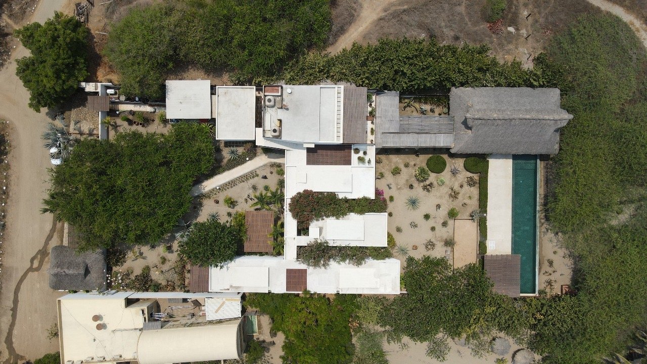 Vista aérea de una propiedad con varias estructuras, árboles y un área de piscina en el patio trasero.