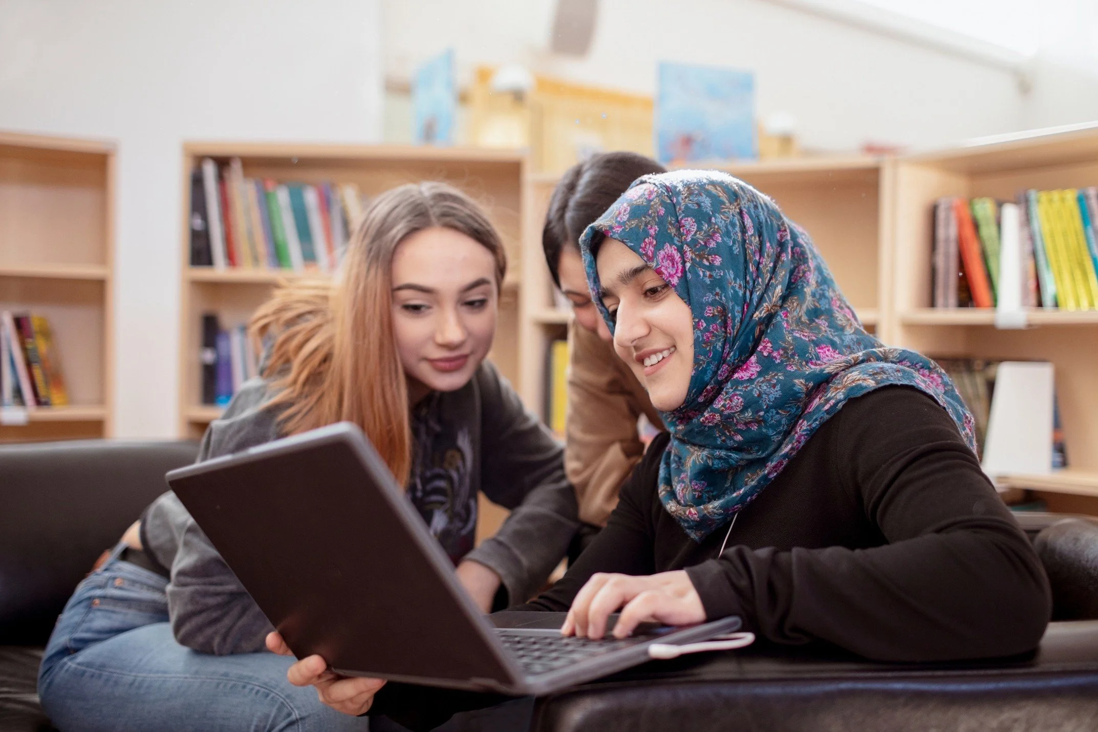 Three young women looking at a laptop in a library.