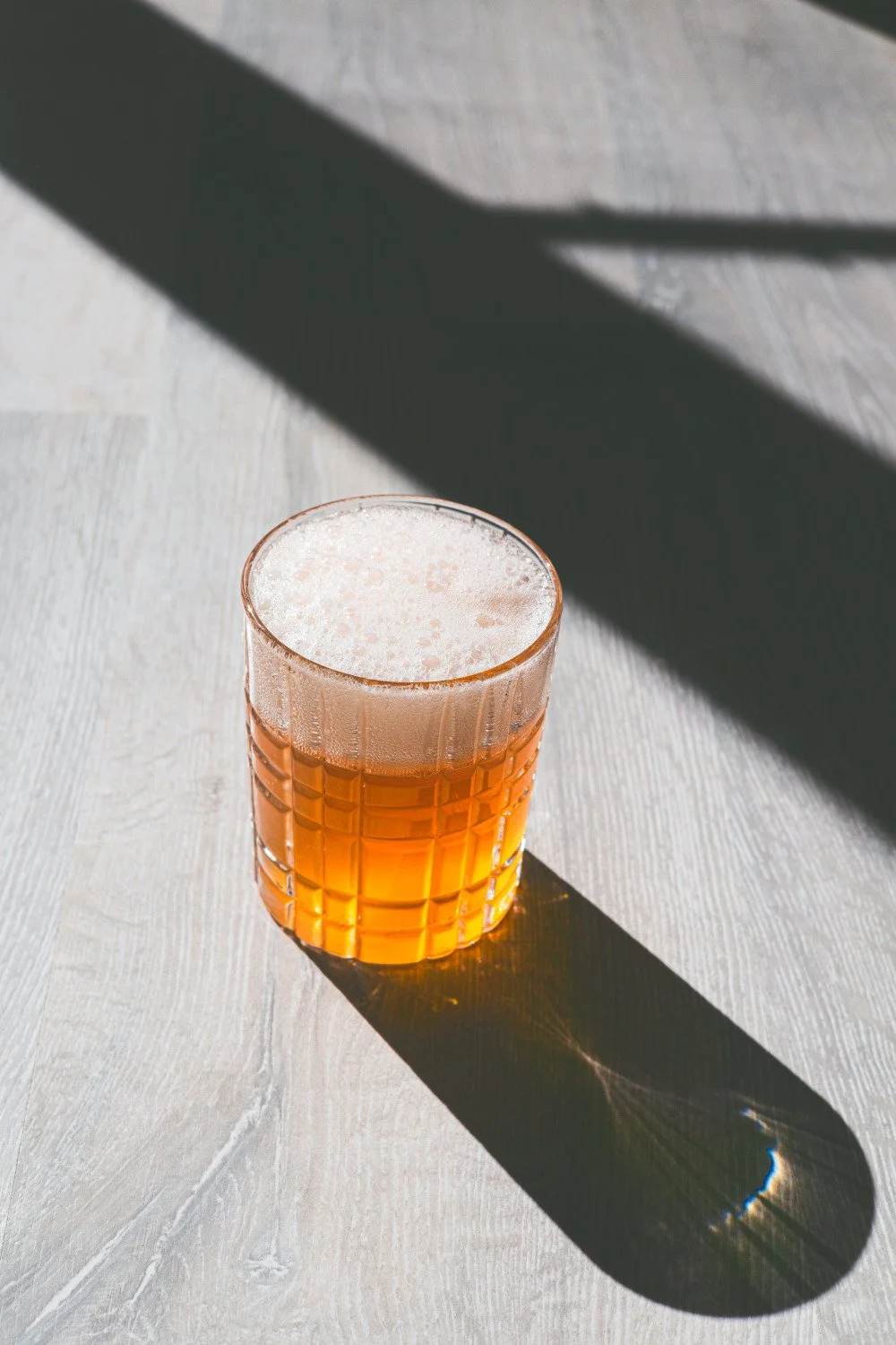 Kombuča stikla glāzē ar putām, fotografēta no augšas ar izteiktu gaismas un ēnas kontrastu