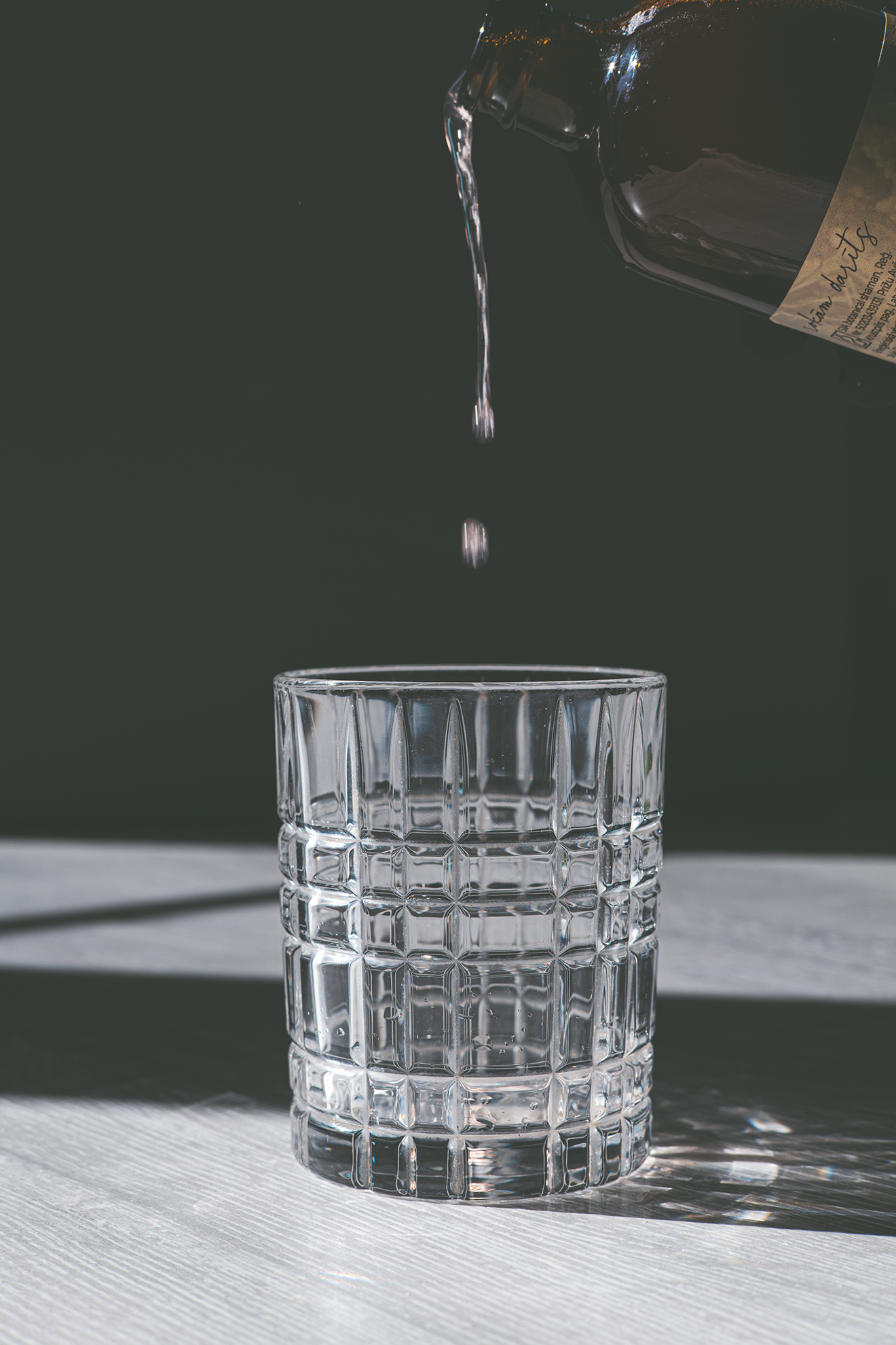 Kombuča tiek lieta stikla glāzē, redzams krītošs piliens dabīgā gaismā