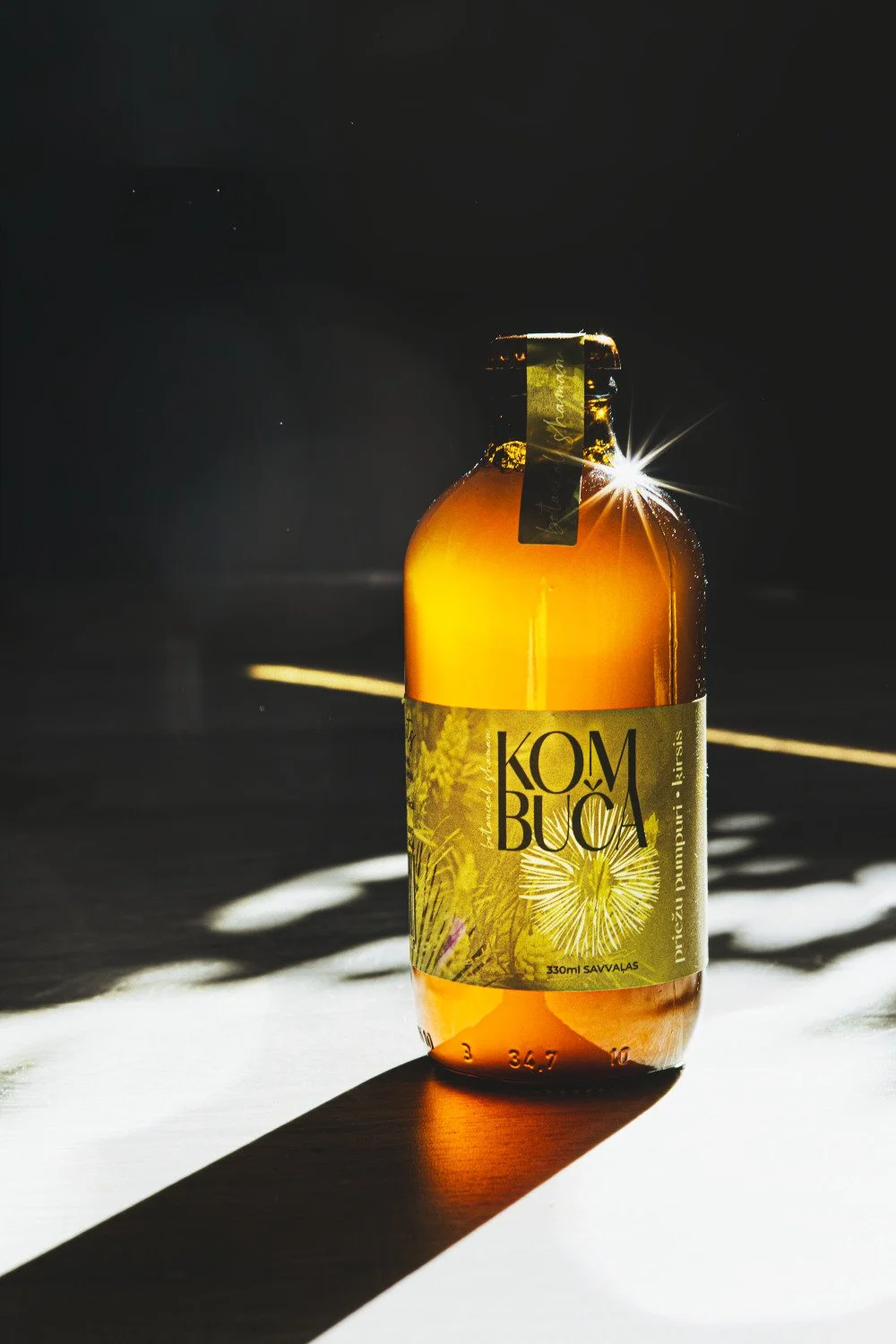 Botanical Shaman kombučas pudele dabīgā saules gaismā ar izteiktām ēnām