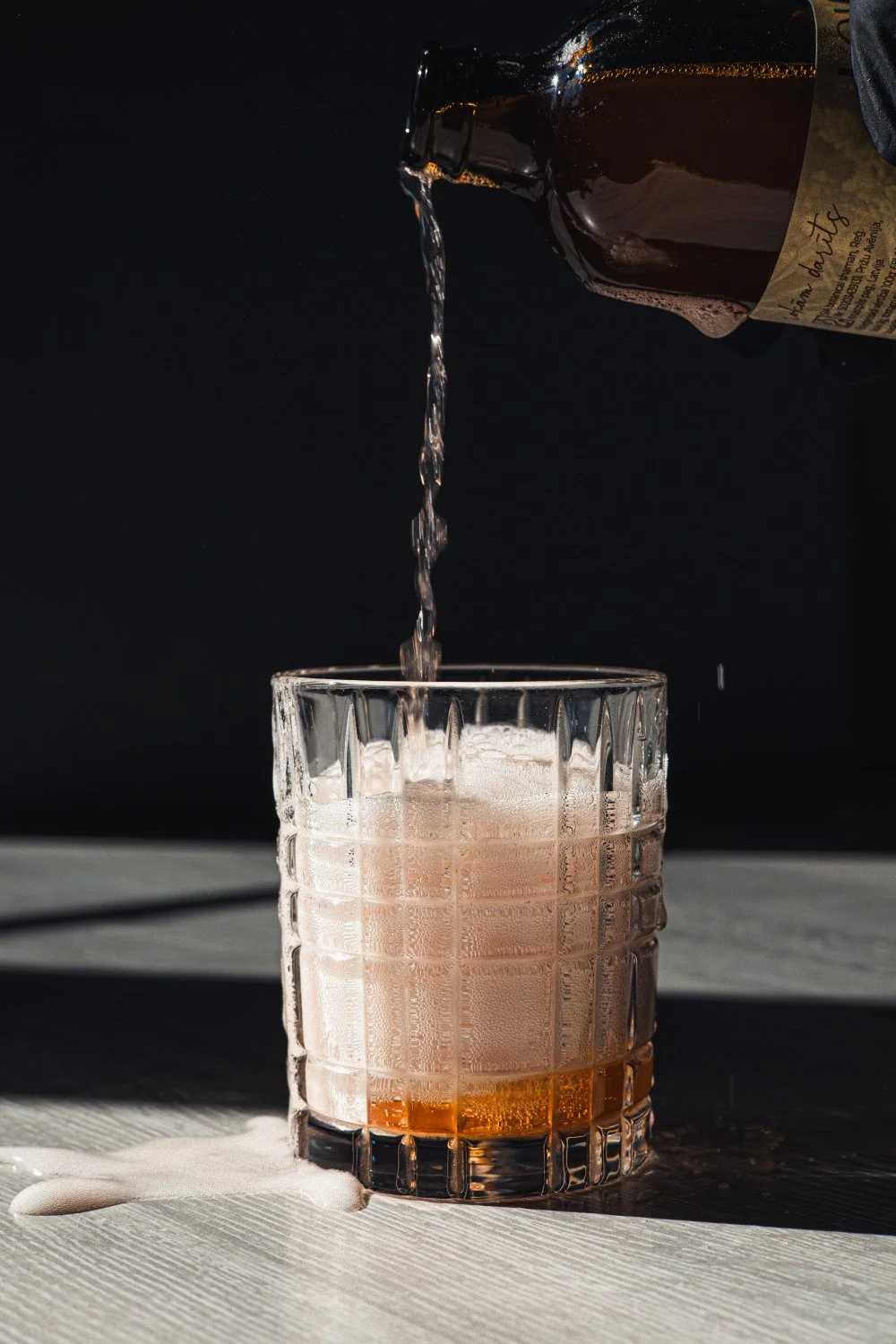 Kombuča tiek lieta stikla glāzē, veidojot putas dabīgā gaismā