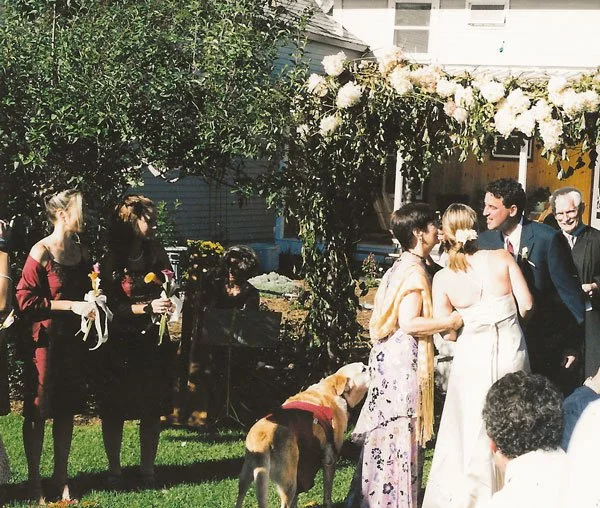 Owners' wedding ceremony outdoors, surrounded by guests, under a floral arch, at their dog friendly Vermont inn