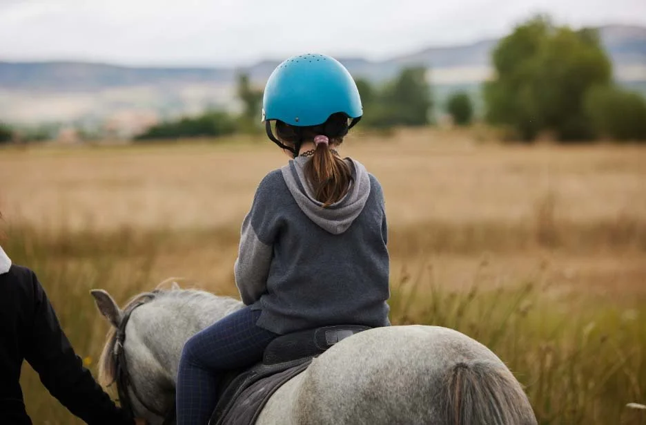 Young girl horseback riding. She is wearing a blue helmet and looking at the Vermont landscape