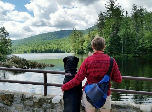Woman with her dog looking out over a lake and Vermont mountains
