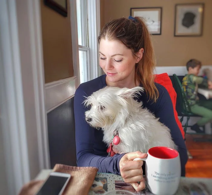 A guest and her small white dog having breakfast in the dining room of The Paw House Inn