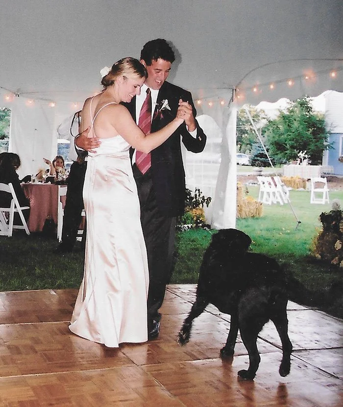 Owners of a dog-friendly Vermont inn dancing at their wedding reception, with a black dog nearby on the dance floor.