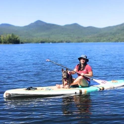 Woman and dog paddle boarding on a lake with Vermont mountains in the background.