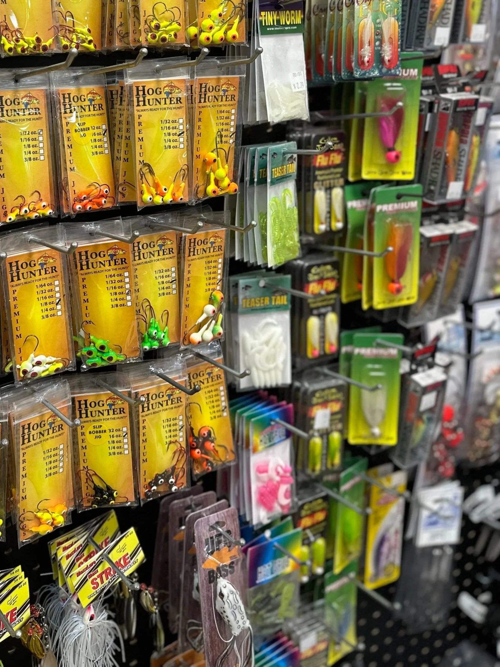 A display of fishing lures and accessories on a store rack, including yellow, orange, green, black, and white soft plastic baits, and various other fishing tackle items.