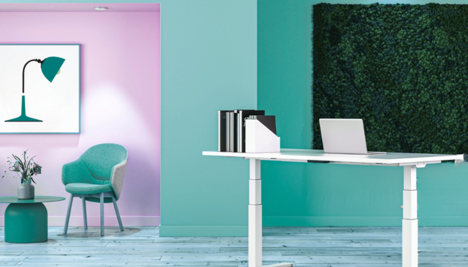 Modern office space with pastel pink and mint green walls, a white desk with a laptop and black binders, a mint green chair, a small round table with a vase and flowers, wall art of a desk lamp, and a green wall art backdrop.