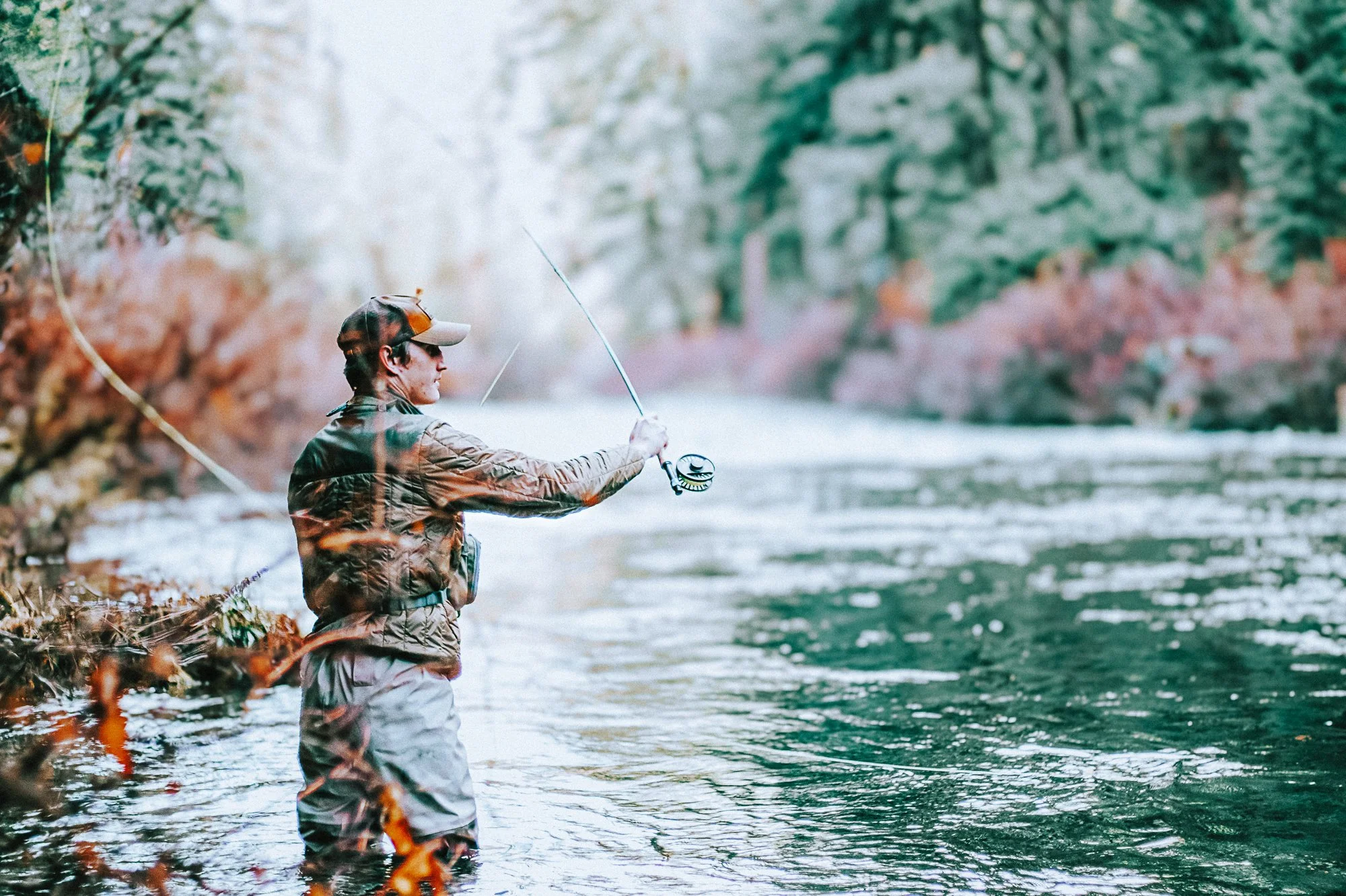 Person fishing in a river surrounded by nature with trees and rocks.