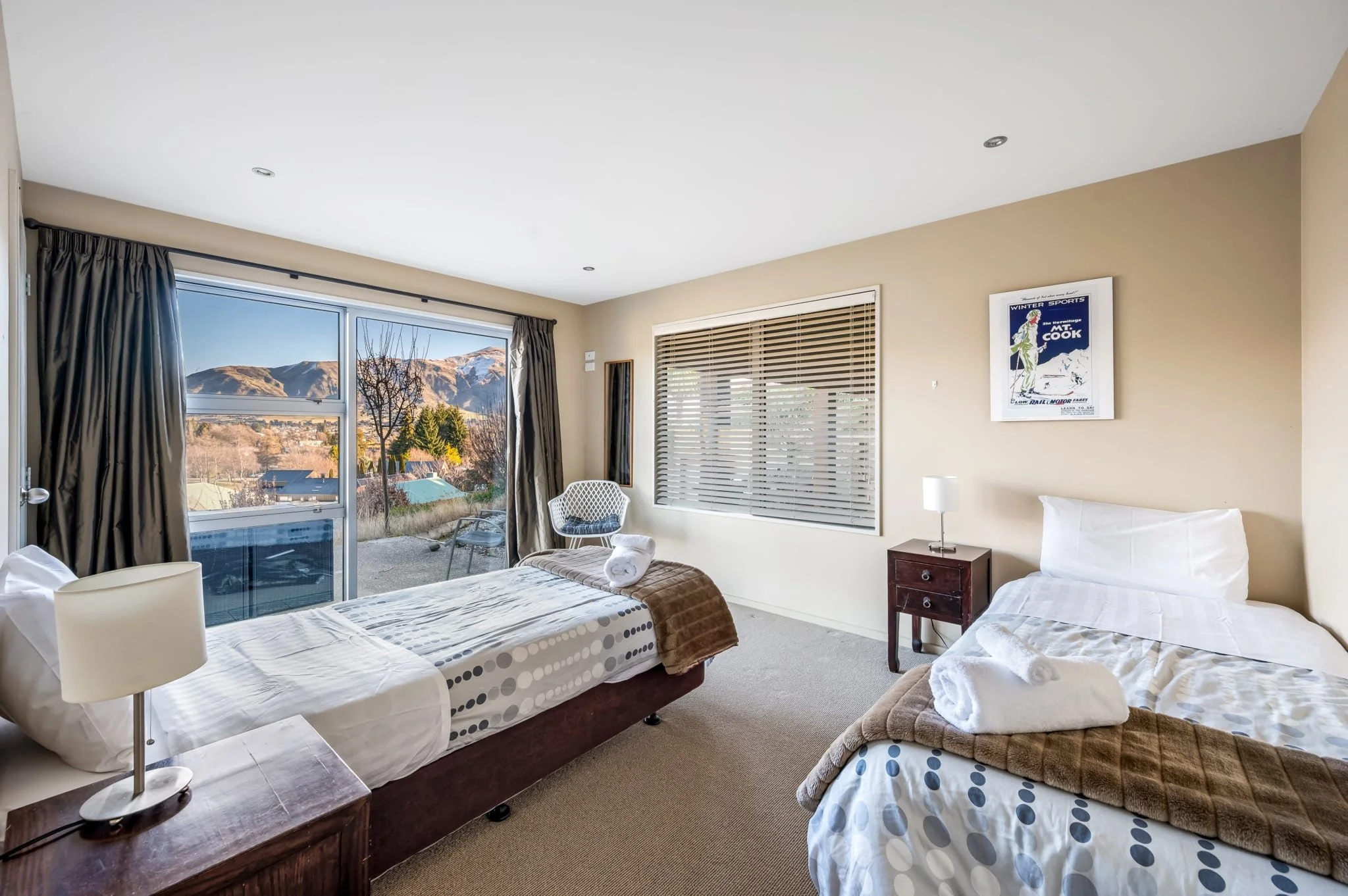 Bedroom room with two beds, a large window showing mountains, and a terrace with outdoor furniture.
