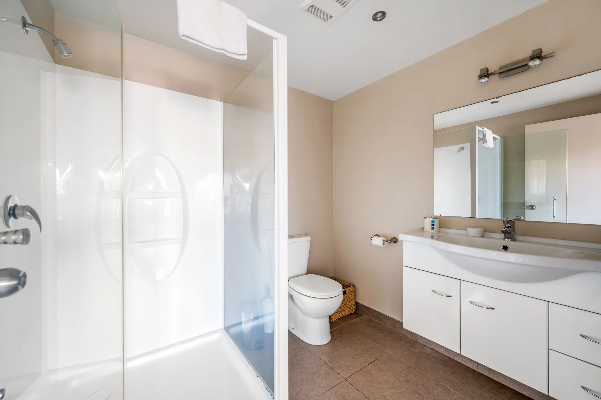 A clean modern tiled bathroom with a walk-in shower on the left, a toilet in the corner, and a white vanity with a large mirror above it on the right.